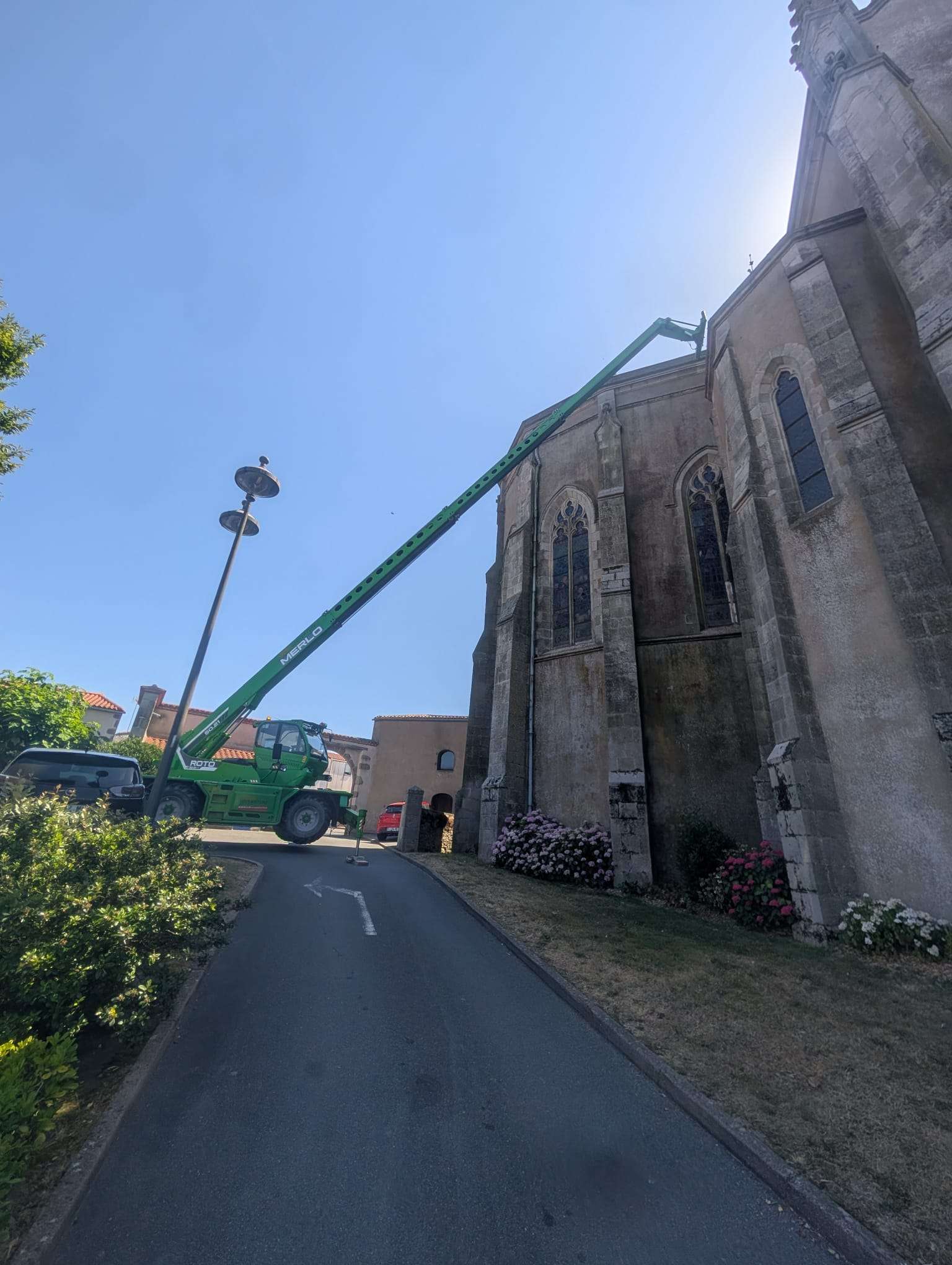 Par une journée ensoleillée, une nacelle télescopique verte s'étend vers la partie supérieure d'une église en pierre.