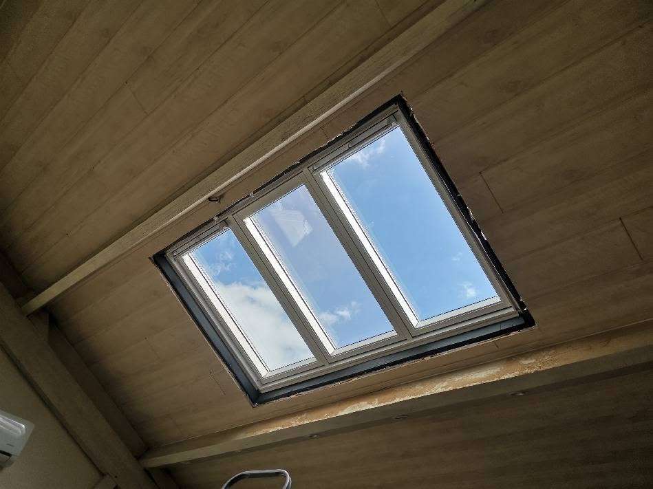Une fenêtre de toit VELUX rectangulaire encastrée dans un plafond en bois, posée avec savoir-faire par un couvreur en Vendée, offrant une vue imprenable sur le ciel bleu et les nuages.